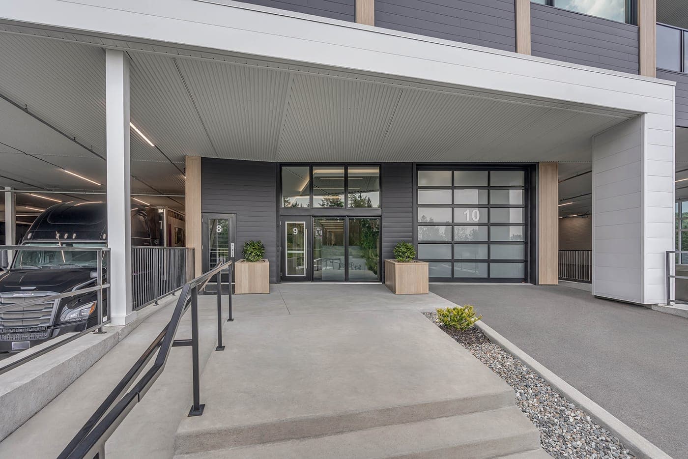 A glazed aluminium sectional door numbered 10 in a grey commercial bay, beside a glass entrance door and a parked transport truck.