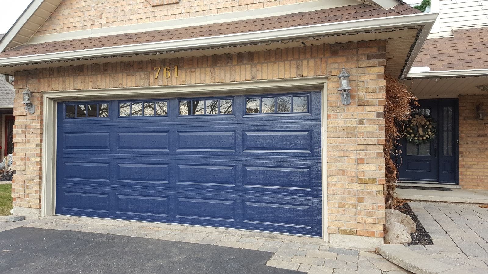 A navy blue long-panel double garage door with a row of windows along the top, on a buff brick house.