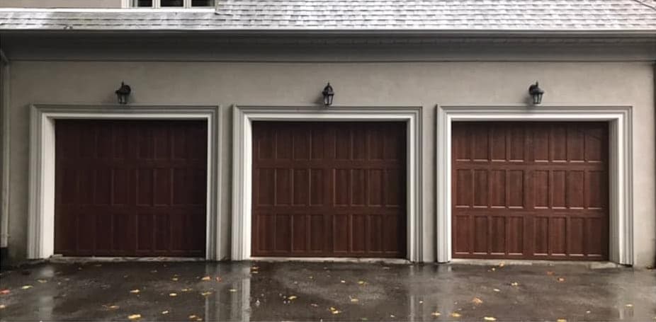 Three woodgrain garage doors with recessed panels, in white-trimmed openings on a stucco house.
