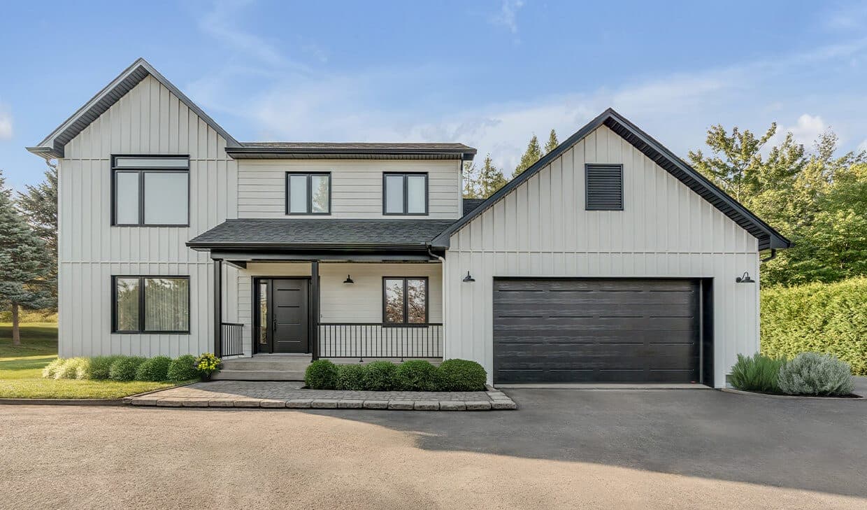 A wide black flush garage door with a faint horizontal grain and no windows, on a white farmhouse-style elevation with black trim.