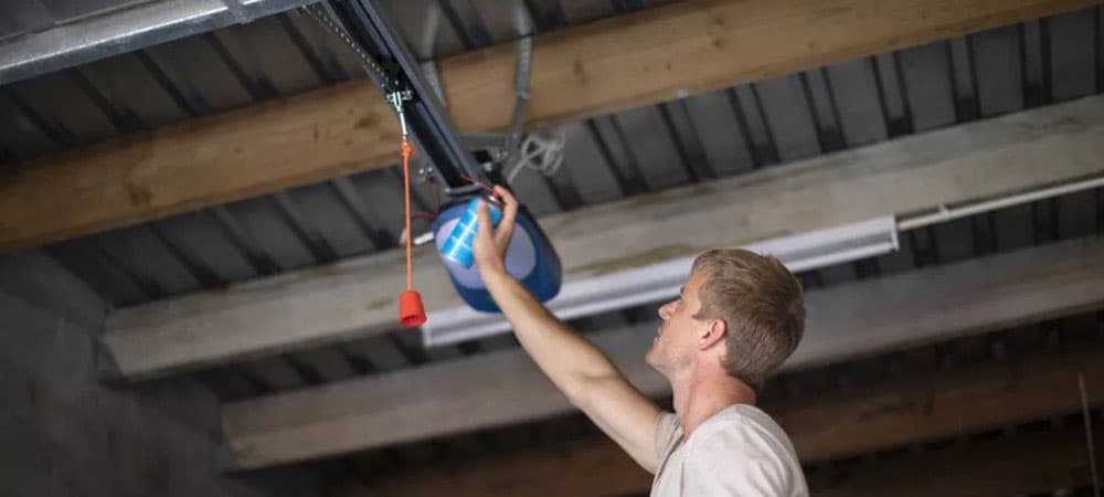 A person reaching up to a ceiling-mounted garage door opener in an unfinished garage.