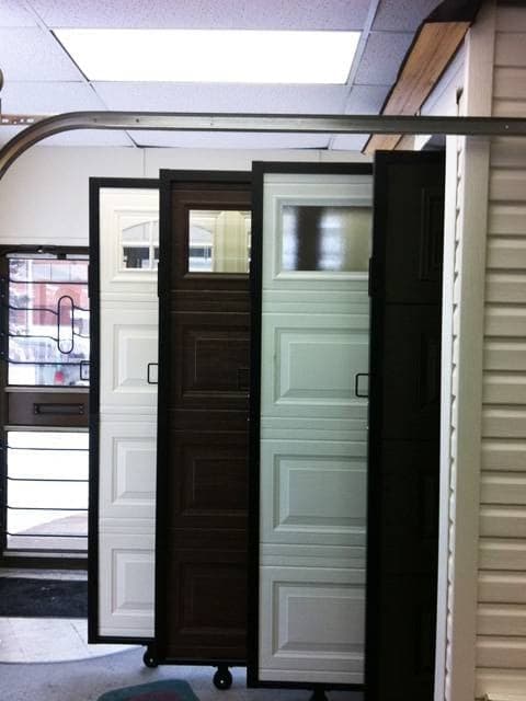 Sample garage door sections in several colours on rolling display stands in the showroom.
