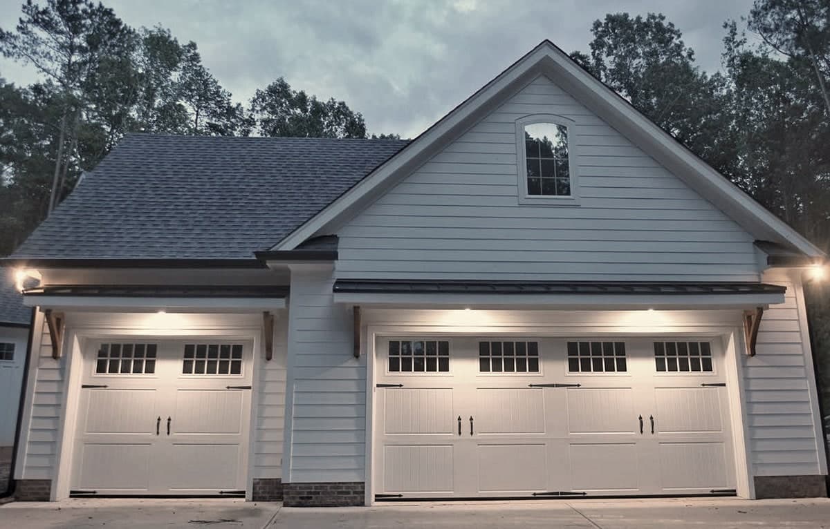 Two white carriage-style garage doors on a detached garage, lit from above at dusk.