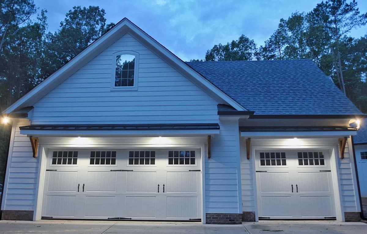 Two white carriage-style garage doors on a detached garage, lit from above at dusk.