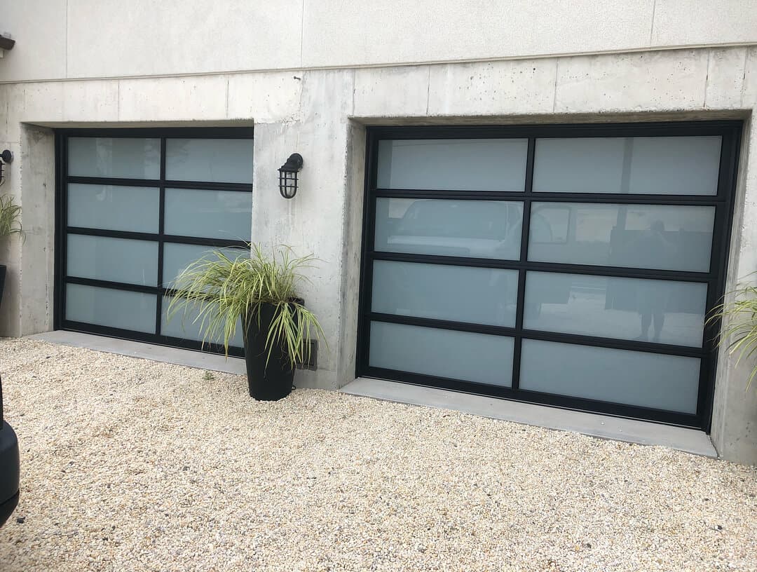Two full-view garage doors with frosted glass panels and black frames on a concrete building.