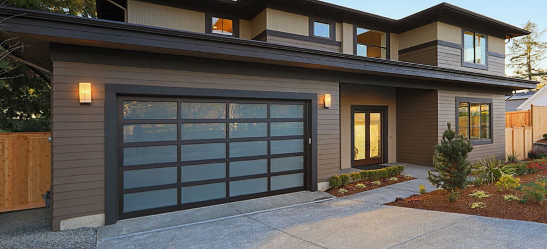 A wide modern garage door with frosted glass panels in a dark frame, on a contemporary house.